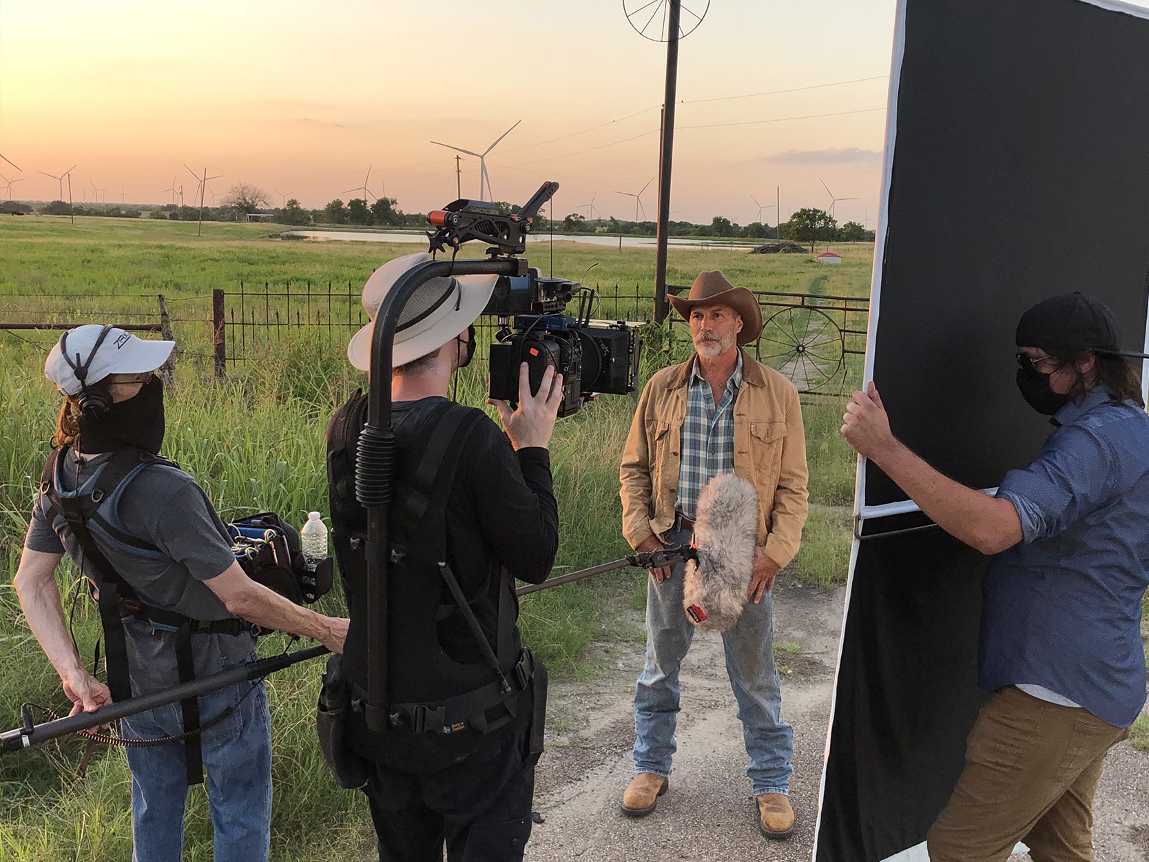 Man on a farm with a cowboy hat being filmed by a professional video production crew.