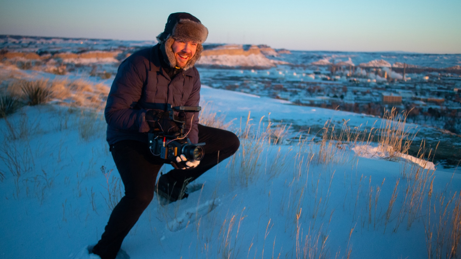 Man smiling and holding a video camera on a snow covered hill.