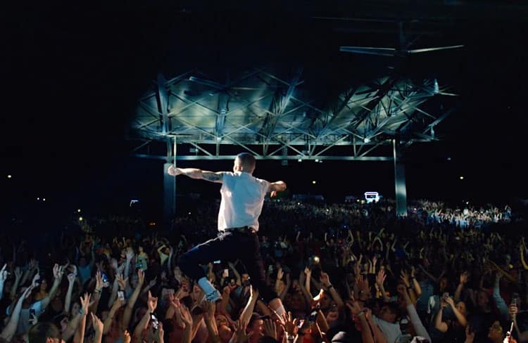 Singer performing in front of a large crowd of people with their hands in the air.