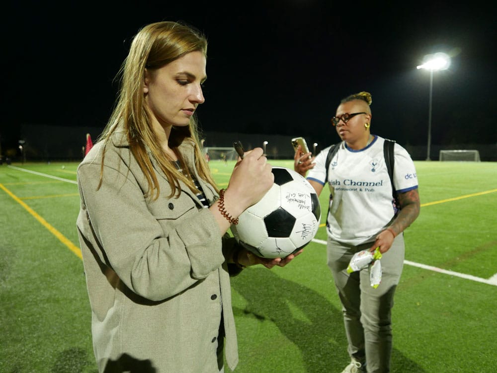 Woman signing a soccer ball on a soccer field.